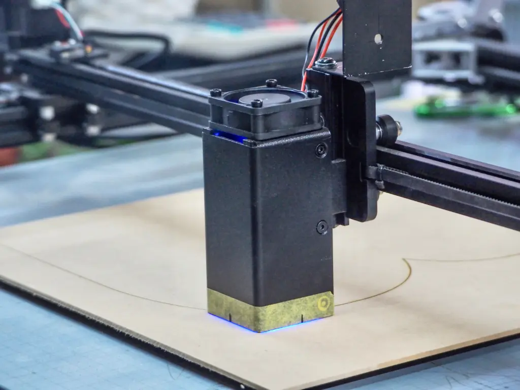 レーザー加工機が木材の板に線を描きながら切断・彫刻を行っている様子